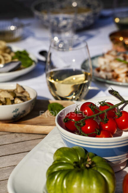 Tavolo esterno con pomodori, pasta con formaggio e pepe, spiedini di gamberi, carciofi e vino bianco — Foto stock