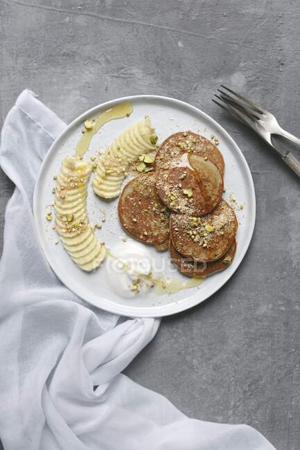 Banana pancakes with coconut yoghurt, pistachios and coconut flakes — Stock Photo