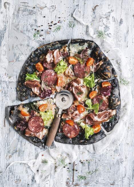Black pizza with ham, sausage, bacon and vegetables — Stock Photo