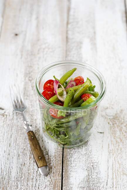 Une salade de haricots et de fusées avec tomates cocktail et oignons dans un verre avec une fourchette — Photo de stock
