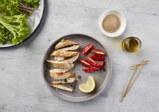 Strisce di pollo su piatto grigio con pomodoro, erbe aromatiche e limone. — Foto stock