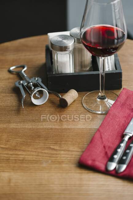 Un bicchiere di vino rosso, un cavatappi, posate, e sale e pepe agitatori su un tavolo — Foto stock