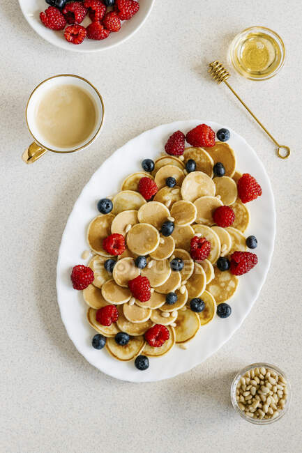 Mini pancakes arranged with berries, pine nuts and agave syrup — Stock Photo