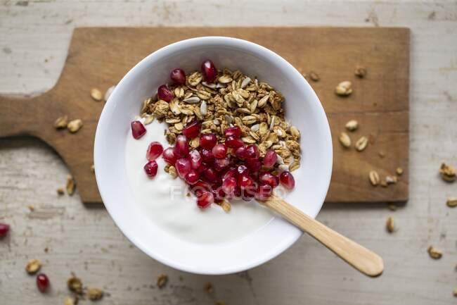 Yoghurt with granola and pomegranate seeds in bowl with wooden spoon — Stock Photo