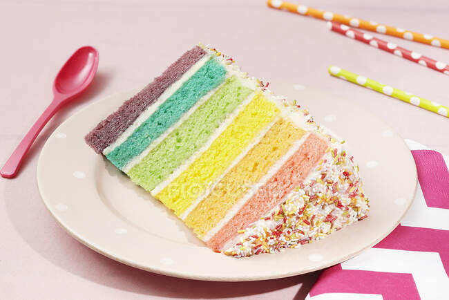 Une tranche de gâteau arc-en-ciel recouverte d'aspersions sur une assiette — Photo de stock