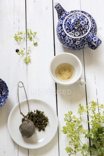Bodegón con una tetera azul y blanca, una taza de té vacía y un colador de té - foto de stock