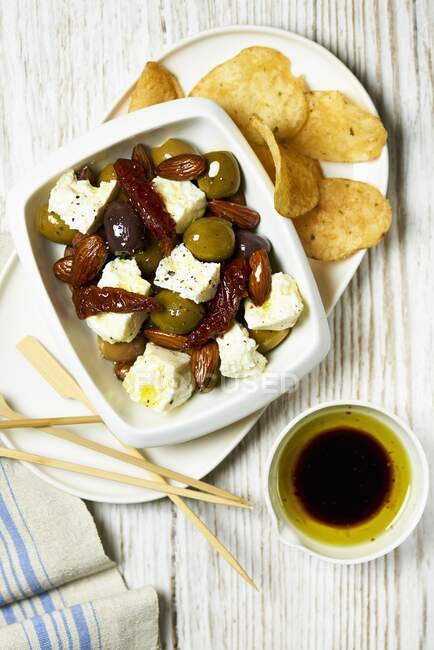 Feta with pickled olives, dried tomatoes, potato chips and olive oil — Stock Photo