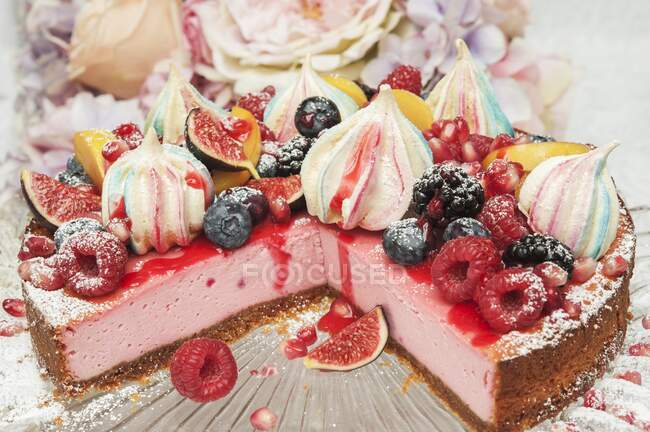 Strawberry cheesecake with meringue kisses and fresh fruit on the top on a glass cake stand in front of flowers — Stock Photo