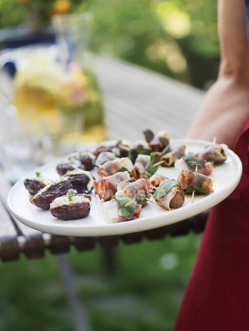 Filled dates and chestnuts wrapped in bacon on a serving plate — Stock Photo