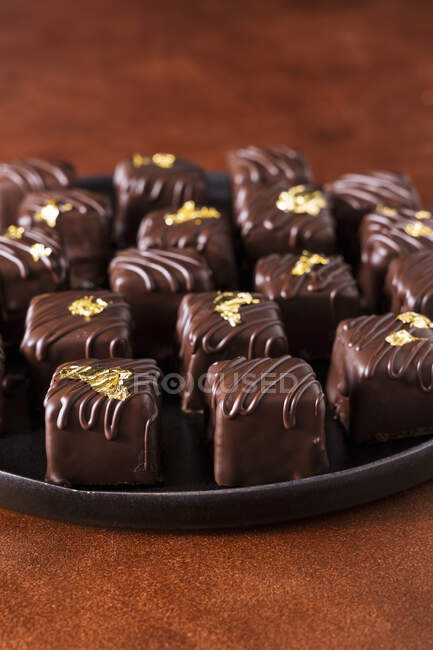Трюфели и пралине из тёмного шоколада, украшенные съедобным золотом — стоковое фото