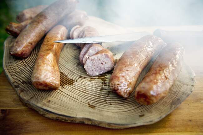 Smoked sausages with a knife on a wooden slab — Stock Photo