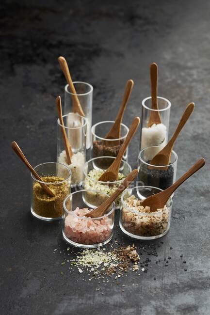 Uma vida tranquila de diferentes variedades de sal em frascos de vidro com colheres de madeira — Fotografia de Stock