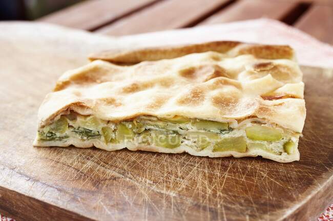 A slice of courgette, egg and quark pie with flaky pastry on a wooden chopping board — Stock Photo