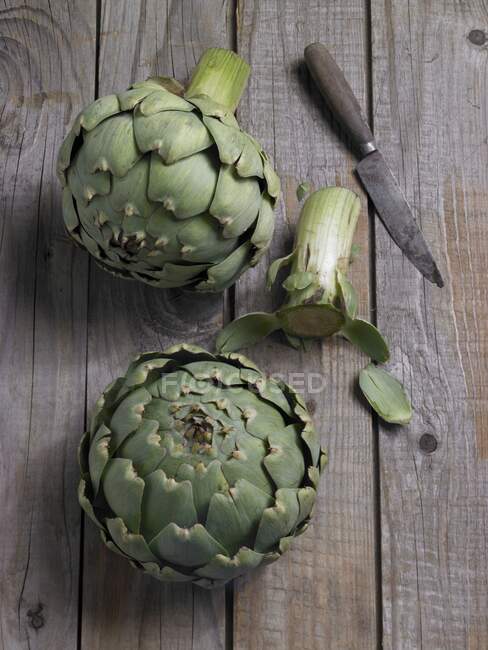 Two fresh artichokes with a knife on a wooden background — Stock Photo