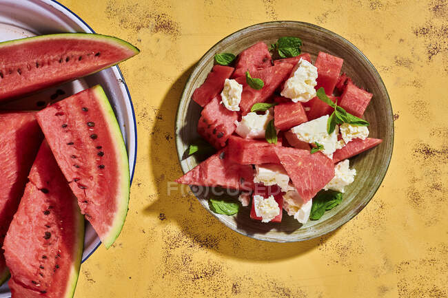Watermelon salad with feta and mint on rustic yellow surface — Stock Photo