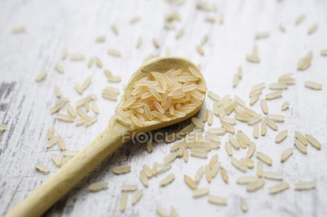 Riz à grains longs sur une cuillère en bois sur un fond en bois — Photo de stock