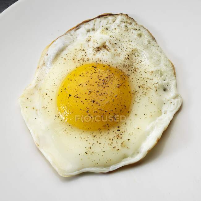 Huevo frito con pimienta negra en plato blanco - foto de stock