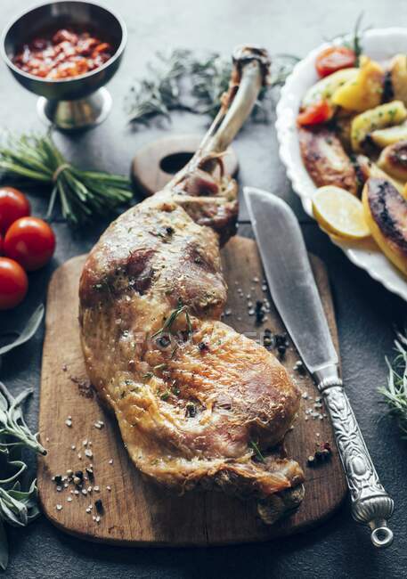 A turkey leg next to a knife on a wooden chopping board — Stock Photo