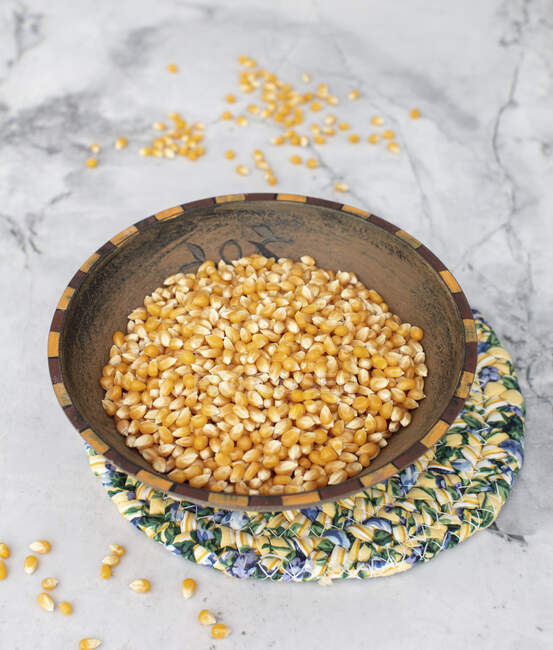 Semillas de maíz crudas en un tazón sobre un fondo blanco - foto de stock
