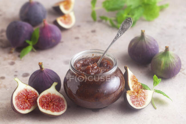 Homemade figs jam in jar and fresh figs on table with green leaves — Stock Photo