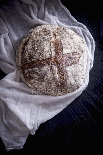 Sourdough bread on muslin cloth at wooden surface — Stock Photo