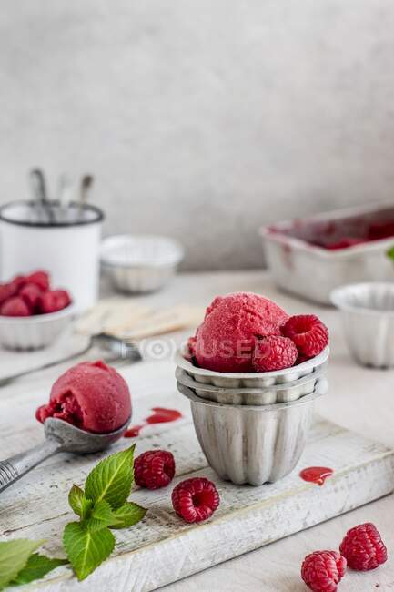 Raspberry sorbet in metal bowls with an ice cream scoop on a wooden board — Stock Photo