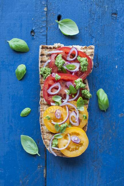 Открытый сэндвич, багет на гриле с желтыми и красными помидорами, базиликовый песто и красный лук — стоковое фото