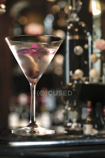 Un cocktail di gin guarnito con un'orchidea rosa, servito in un bicchiere da martini in un bar — Foto stock