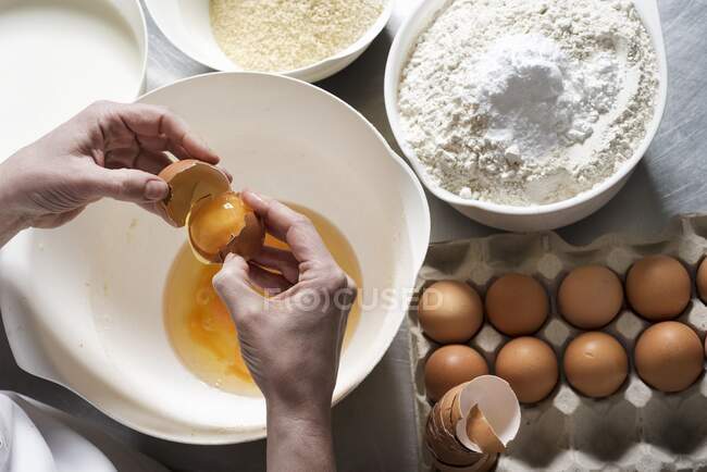 Hands breaking eggs over a bowl with almond flour and regular flour with baking powder next to it — Stock Photo