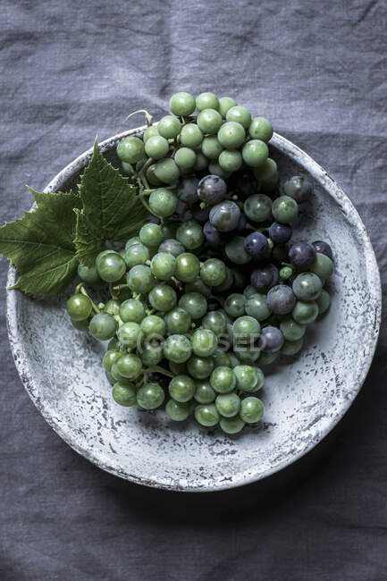 Uvas frescas colhidas em tigela de cerâmica em toalha de mesa cinza — Fotografia de Stock