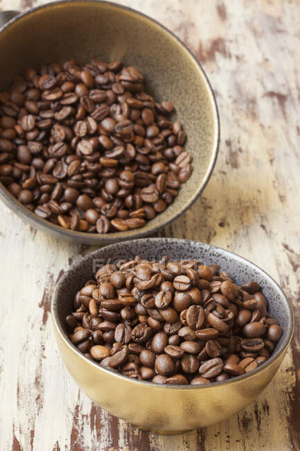 Granos de café en un tazón de madera sobre un fondo marrón - foto de stock
