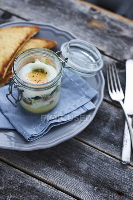 Huevo en frasco de vidrio servido con pan tostado - foto de stock