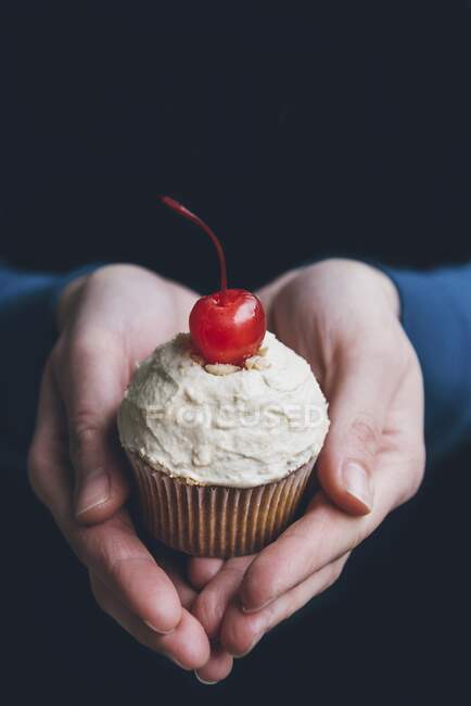 Mains tenant un cupcake avec glaçage aux arachides et un cocktail cerise — Photo de stock