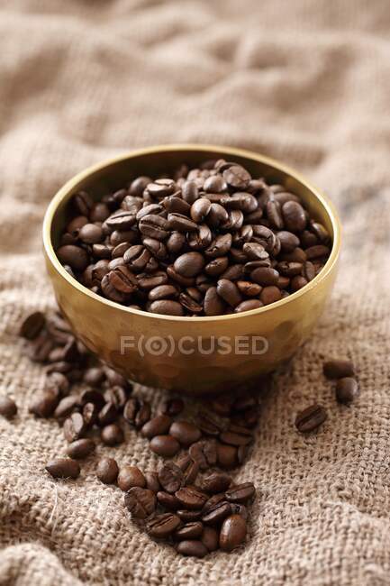 Grãos de café em uma tigela de metal em um pano de juta — Fotografia de Stock