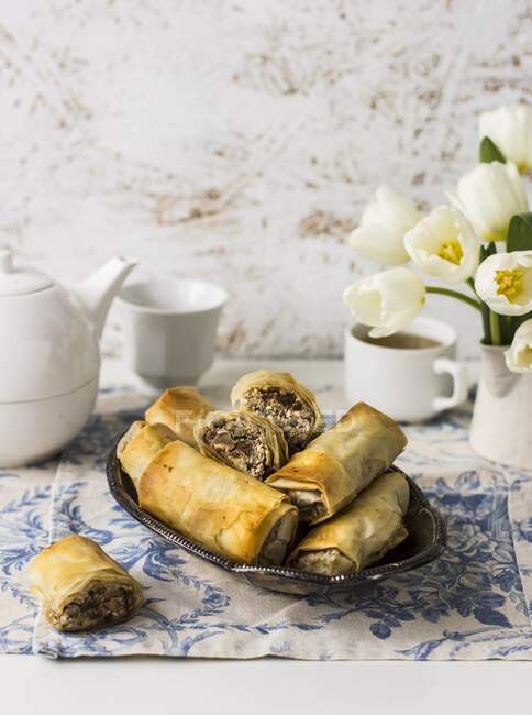 Rolos de filo com queijo Manouri, nozes, passas e hortelã; chá, tulipas brancas — Fotografia de Stock