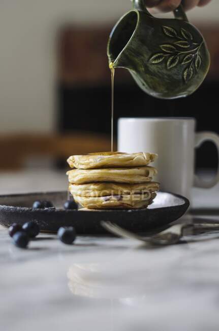Syrup pouring from a jug onto a pile of pancakes — Stock Photo
