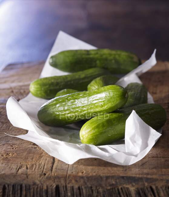 Mini cucumbers on paper and an old wooden board — Stock Photo