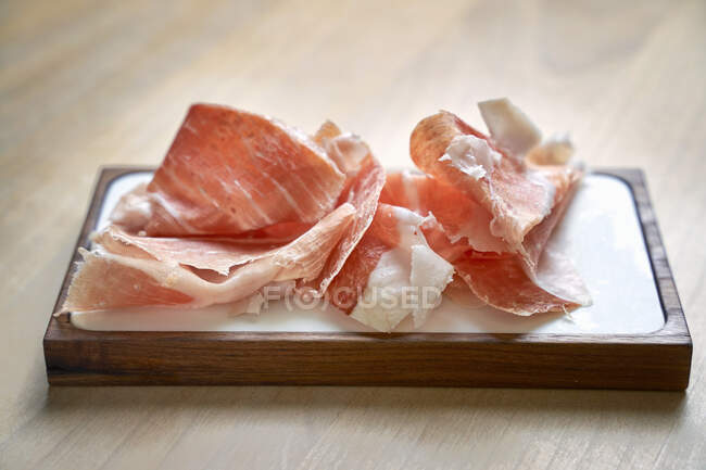 Sliced prosciutto on wooden board — Stock Photo