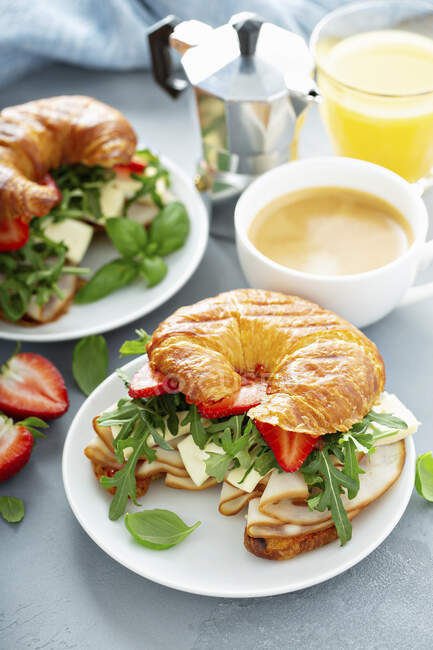 Sandwich de desayuno en un croissant con pavo, rúcula, fresas y brie - foto de stock