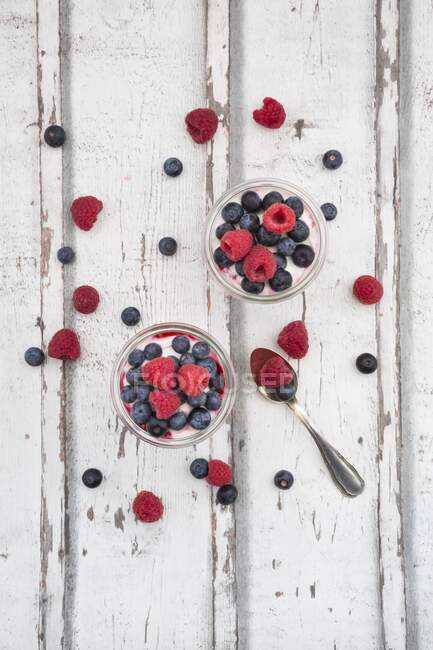 Yaourt grec avec gelée de fruits et framboises et bleuets frais sur la surface en bois — Photo de stock
