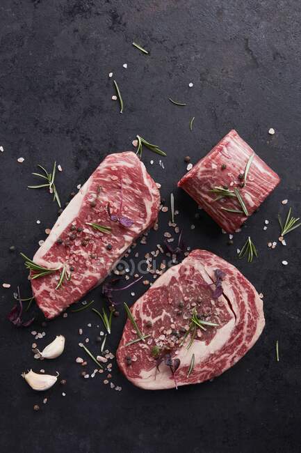 Various beef steaks with herbs and spices on a black background — Stock Photo