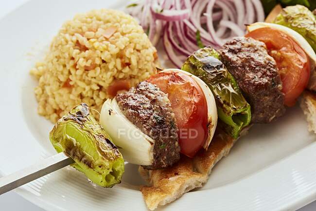 Pincho de carne picada con cebolla, pimiento verde y tomate servido con arroz y pan plano - foto de stock