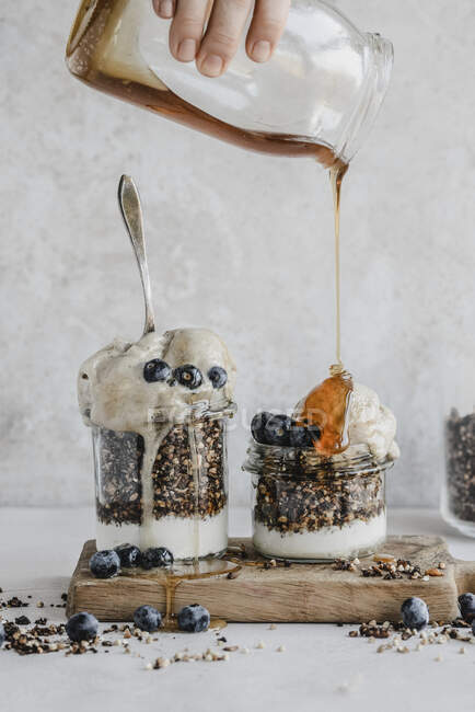 Granola with yogurt in a jar with blueberries banana ice cream topped with maple syrup — Stock Photo