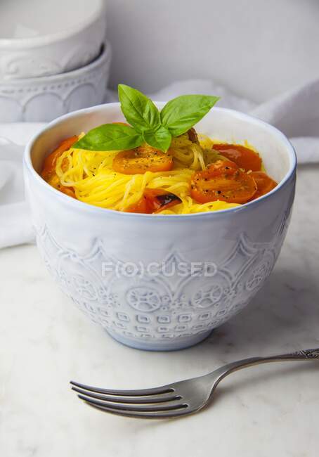 Pasta capellini sin gluten con tomates asados y albahaca en un tazón - foto de stock