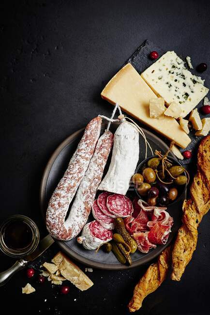 A mixed antipasti platter with olives, capers, prosciutto, dried sausage, salami, grissini, parmesan and blue cheese — Stock Photo