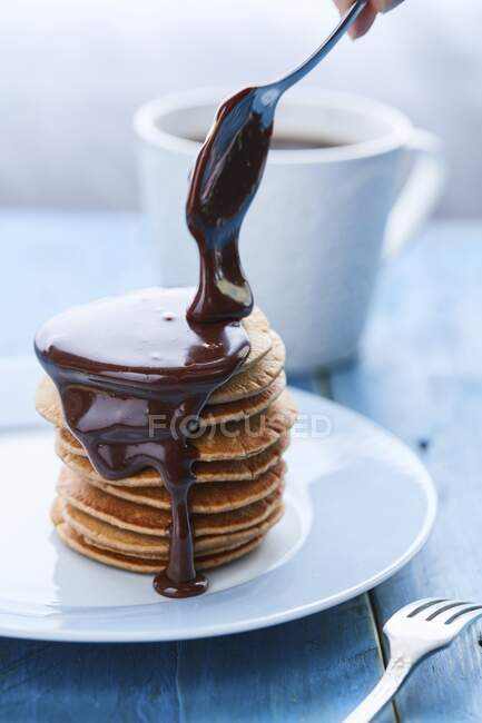 Molho de chocolate pingando de uma colher sobre uma pilha de panquecas — Fotografia de Stock