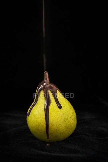 Melted chocolate flowing over a pear against a black background — Stock Photo