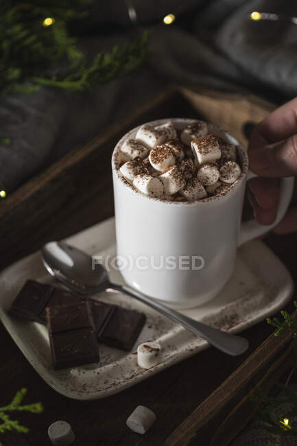 Hand holding a cup of hot drink with marshmallow with Christmas lights — Stock Photo