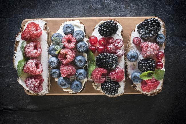 Bruschettas with berries and cream cheese on wooden board — Stock Photo