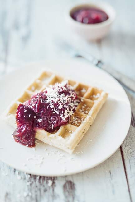 A Belgian waffle with plum compote and coconut chips — Stock Photo